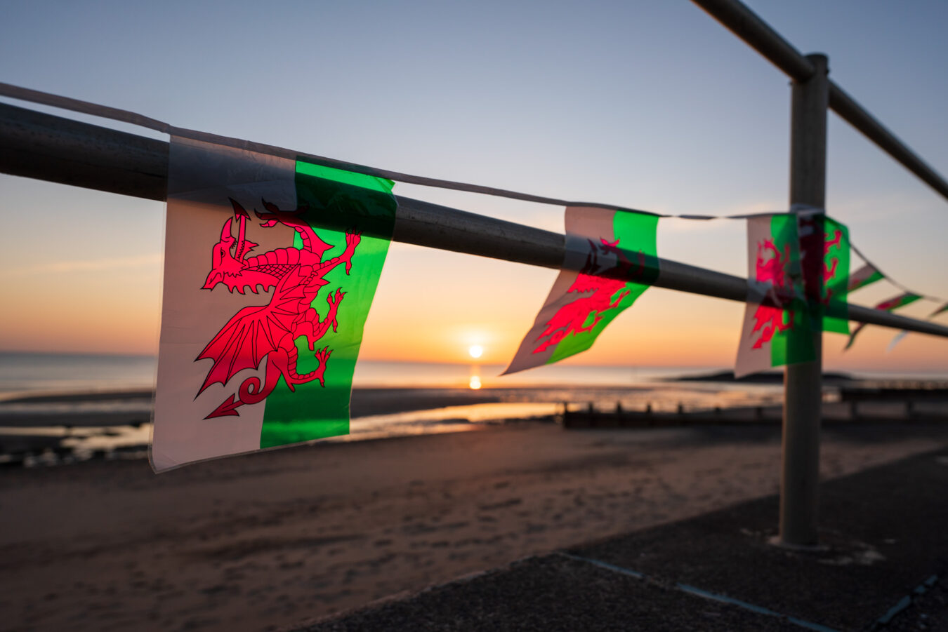 Small Welsh flags running along a sea promenade at sunset