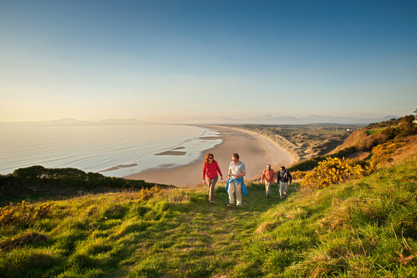 People walking up the hill with Harlech beach in the background