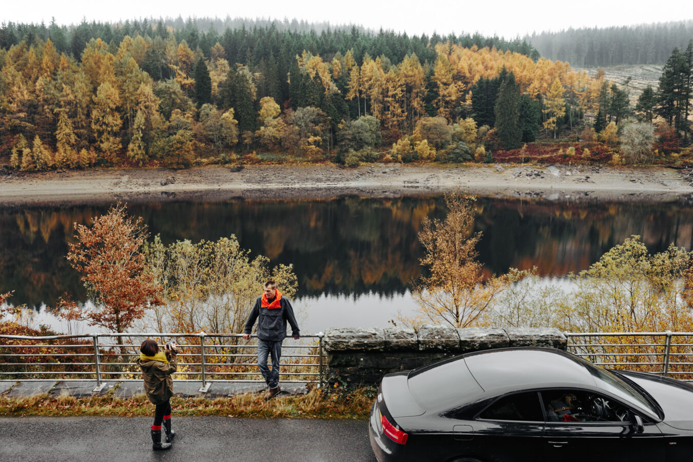 Couple taking a picture by the side of the road, with autumn colours in the background